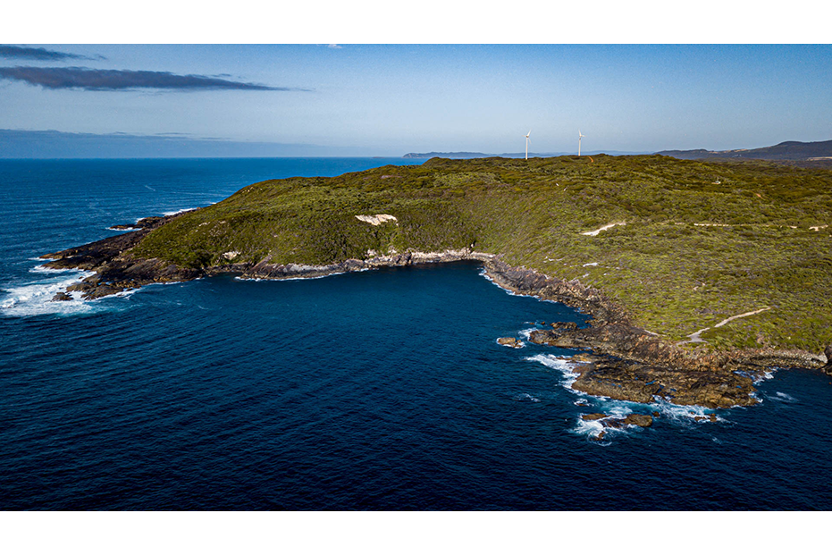 A photo showing the turbines in the distance on the headland with the ocean in the foreground.